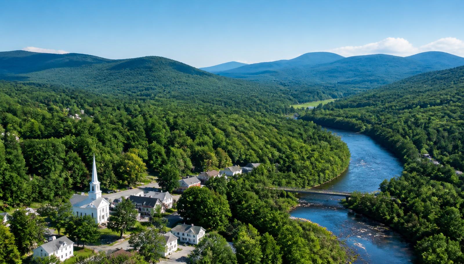 Aerial view of a New Hampshire river valley with a white church steeple and forested hills