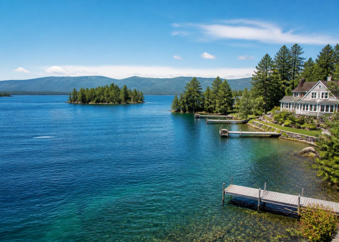 Lake Winnipesaukee in summer with a wooden dock, pine islands and a shingled lakefront house