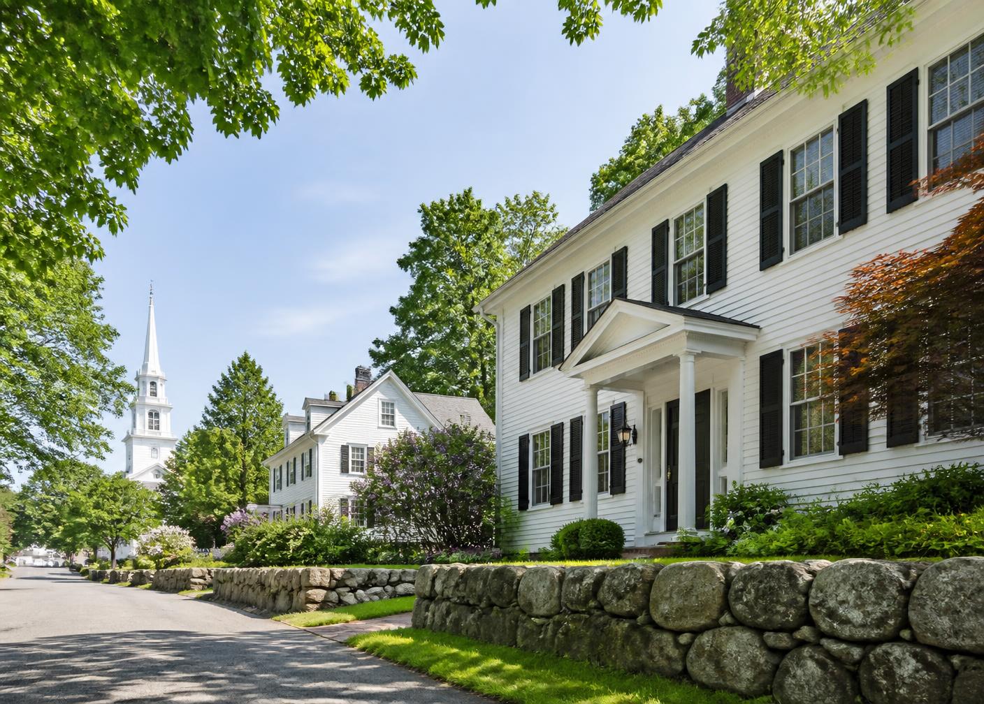 White colonial homes with black shutters and stone walls on a tree-lined southern New Hampshire street